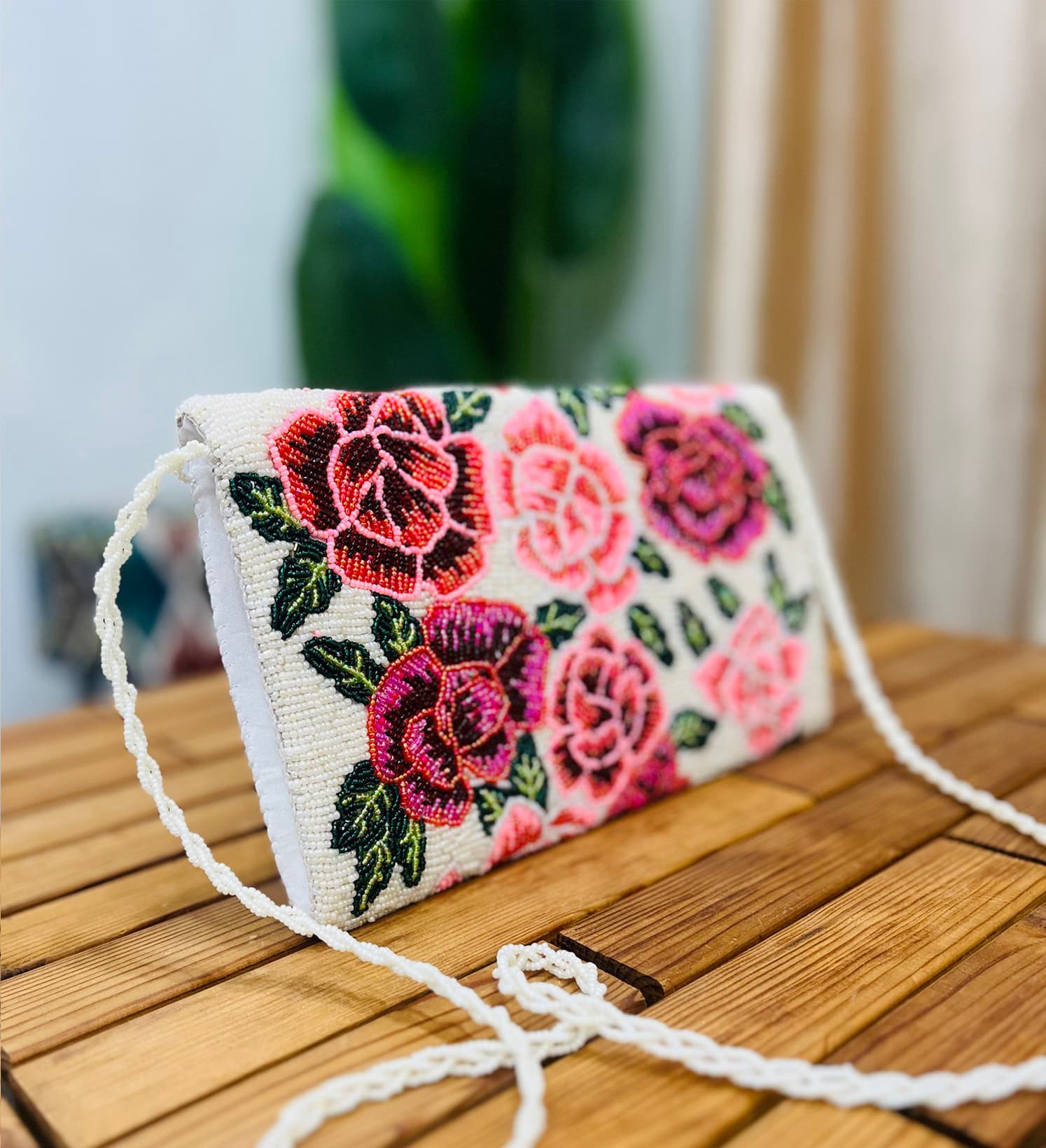 A vibrant hand-beaded clutch with intricate floral rose designs, displayed against a plain white background.