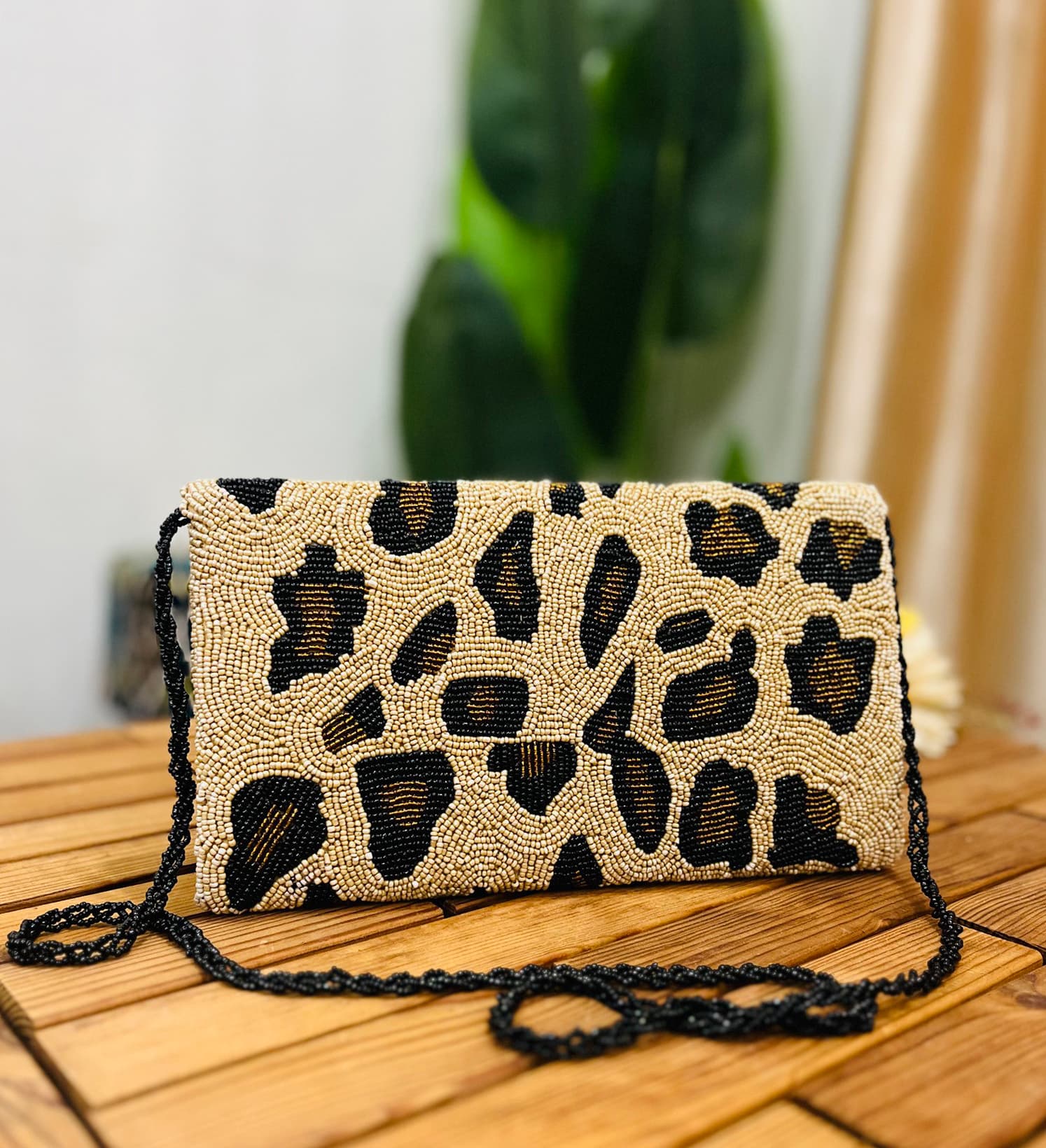 Leopard print clutch with black, brown, and gold beads, featuring a gold zipper and a label tag on a white background.