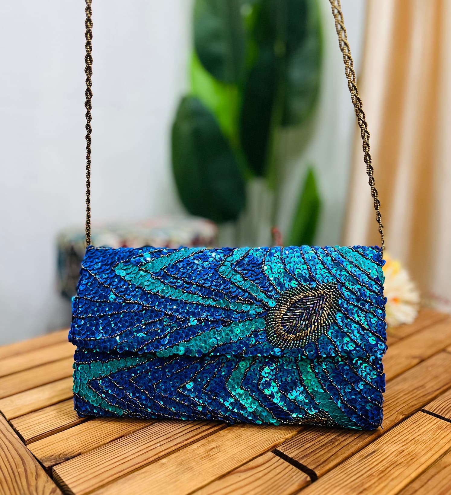Intricately designed envelope clutch adorned with vibrant peacock feather motifs using sequins and beads on a dark