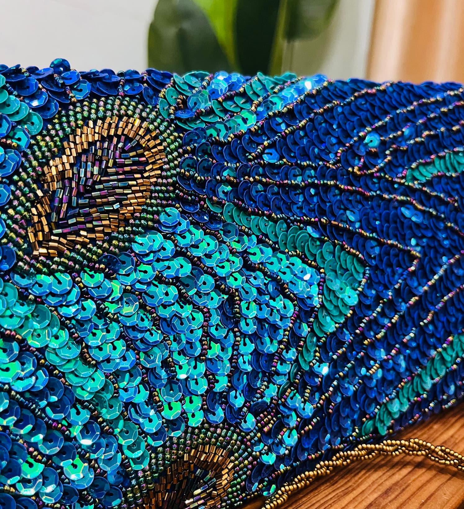 A colorful clutch with a peacock feather design, adorned with sequins and beads, set against a plain background.
