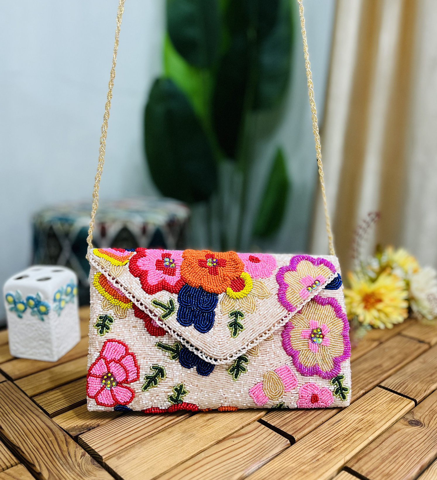 Beaded clutch with floral design in red, black, and gold beads, set against a cream background. Labeled "Zara" at the back.