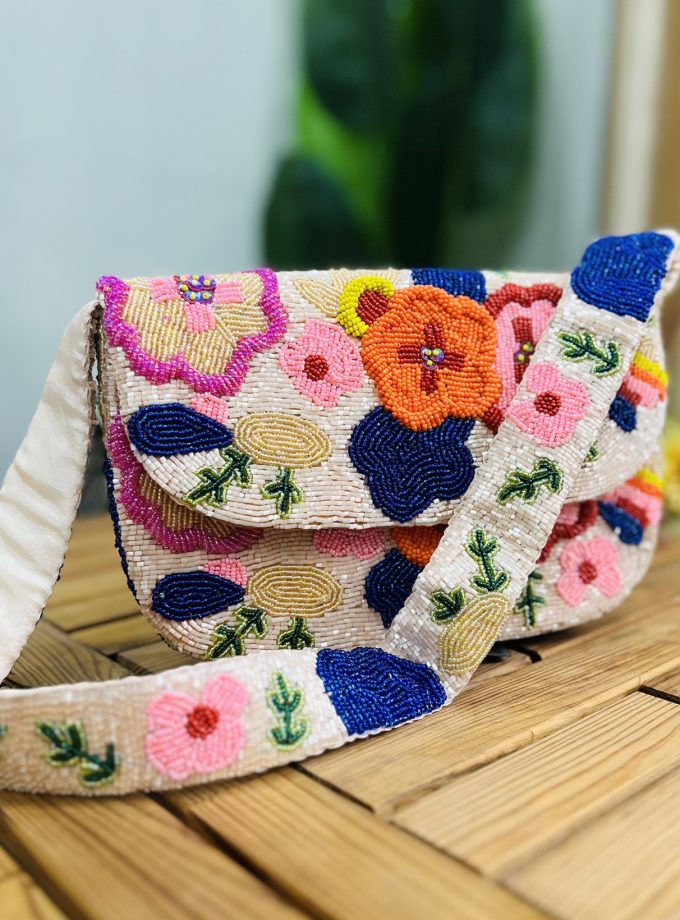 A colorful hand-beaded shoulder bag with pink, green, and gold floral patterns, adorned with green and gold bead tassels.