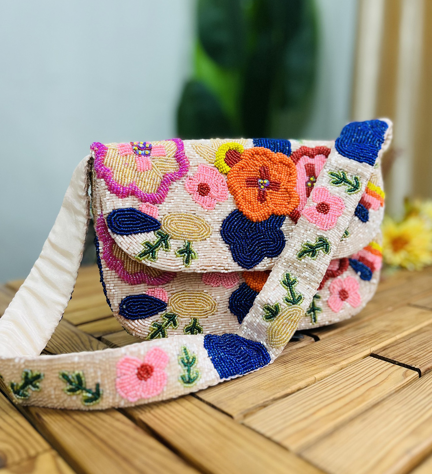 A colorful hand-beaded shoulder bag with pink, green, and gold floral patterns, adorned with green and gold bead tassels.