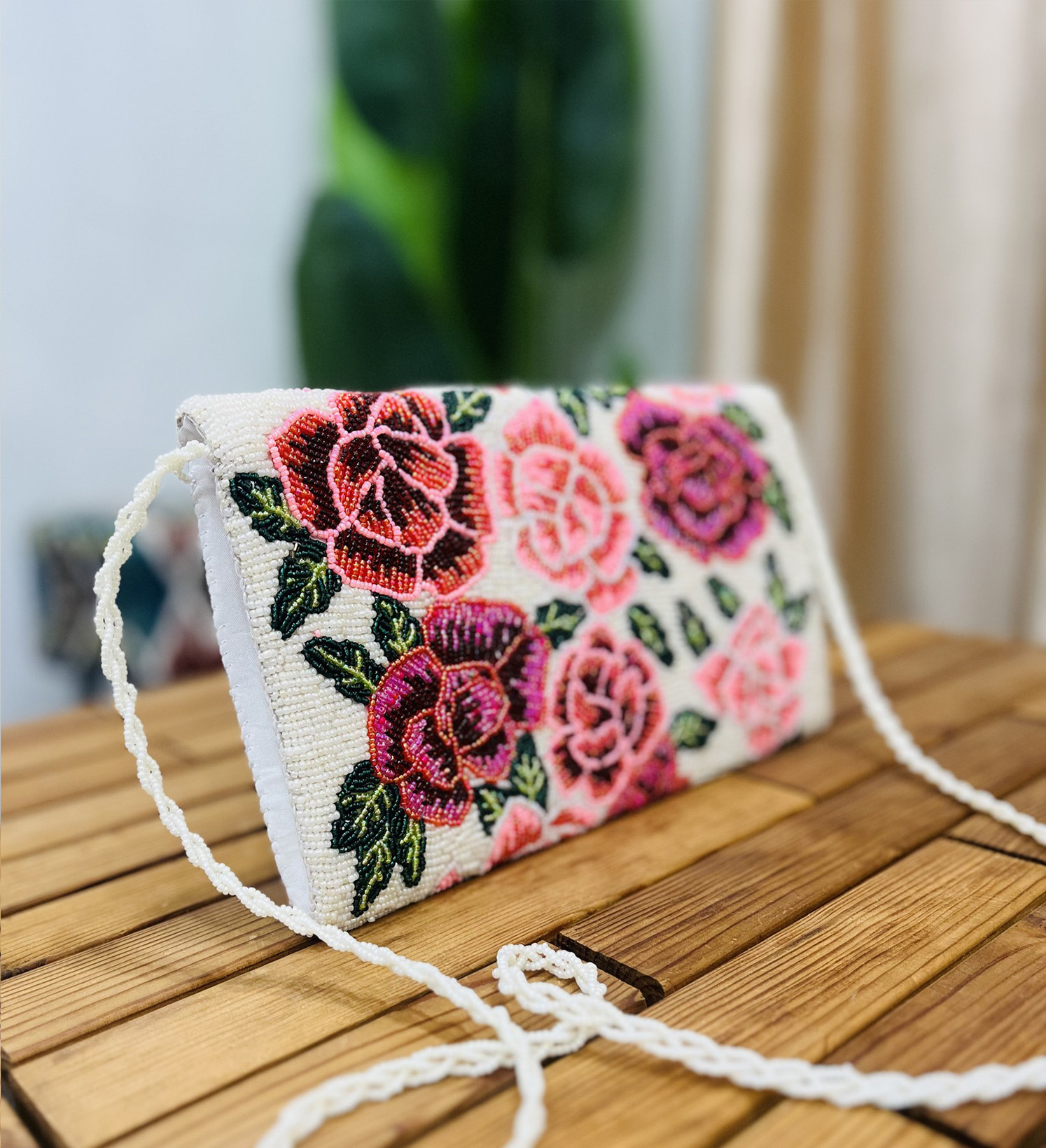 A vibrant hand-beaded clutch with intricate floral rose designs, displayed against a plain white background.
