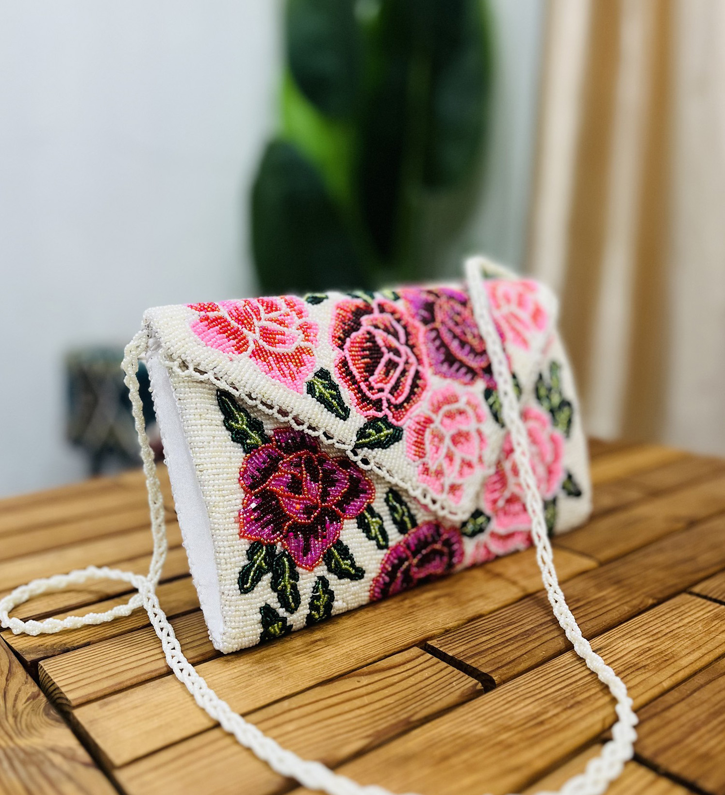 White clutch with intricate pink and green floral rose beadwork, gold chain strap, and decorative fringe detailing.