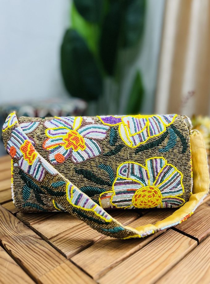Gold shoulder bag adorned with intricate floral beadwork, featuring a structured design and chain strap, set against a plain