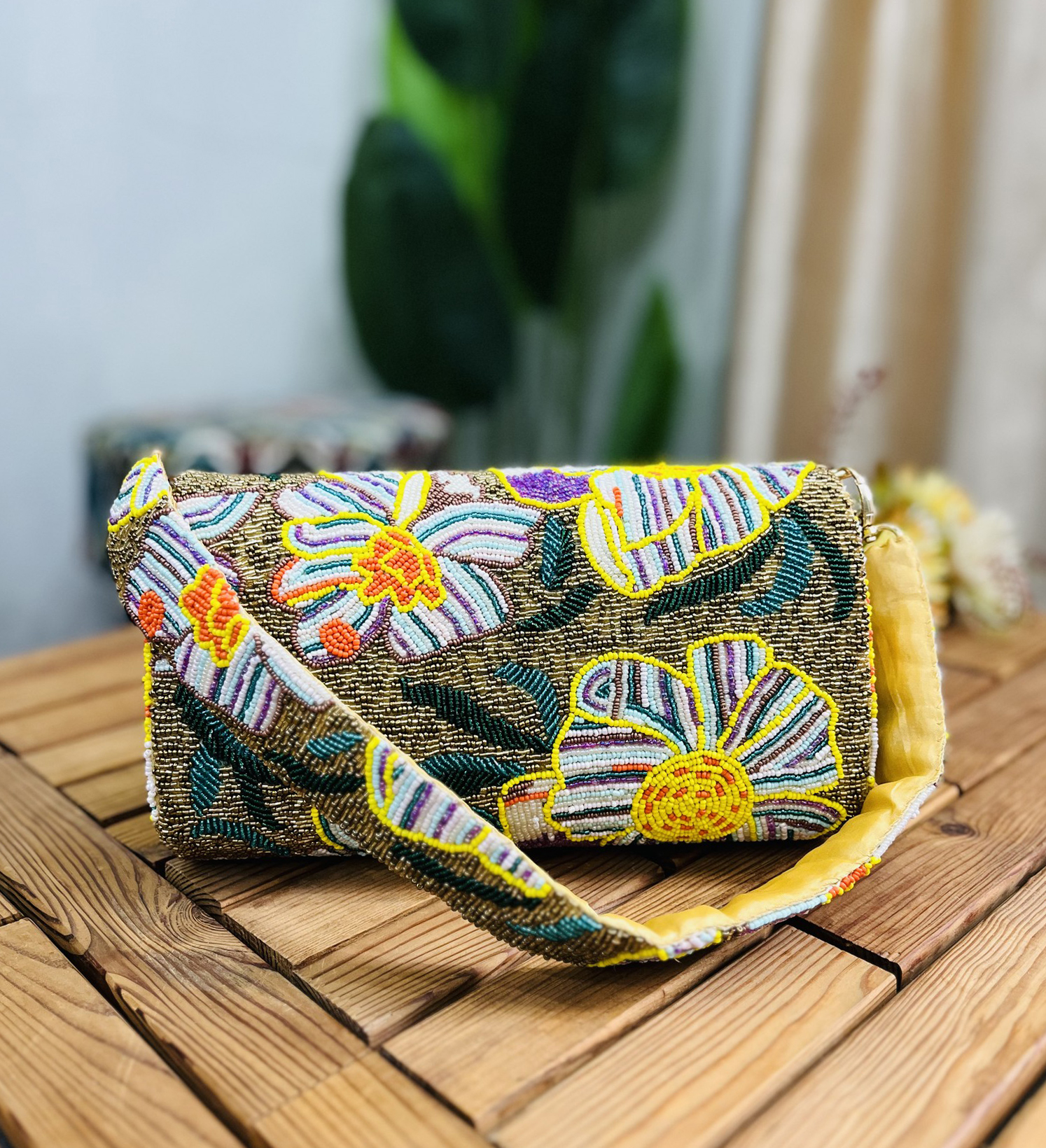 Gold shoulder bag adorned with intricate floral beadwork, featuring a structured design and chain strap, set against a plain