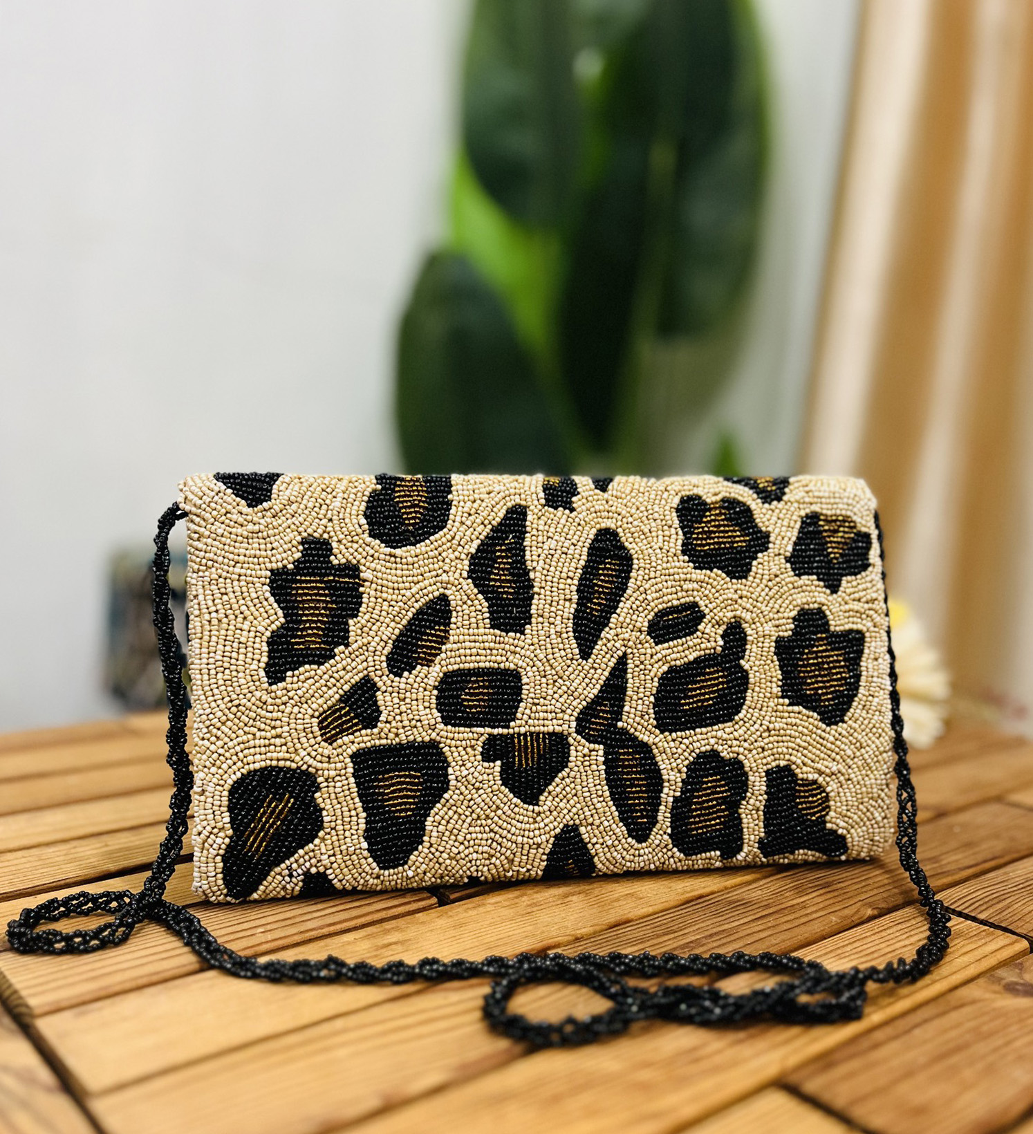 Leopard print clutch with black, brown, and gold beads, featuring a gold zipper and a label tag on a white background.