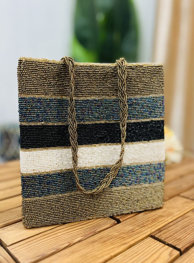 Colorful tote bag with metallic stripes, hand-beaded design, and beige handles, displayed on a plain white background.