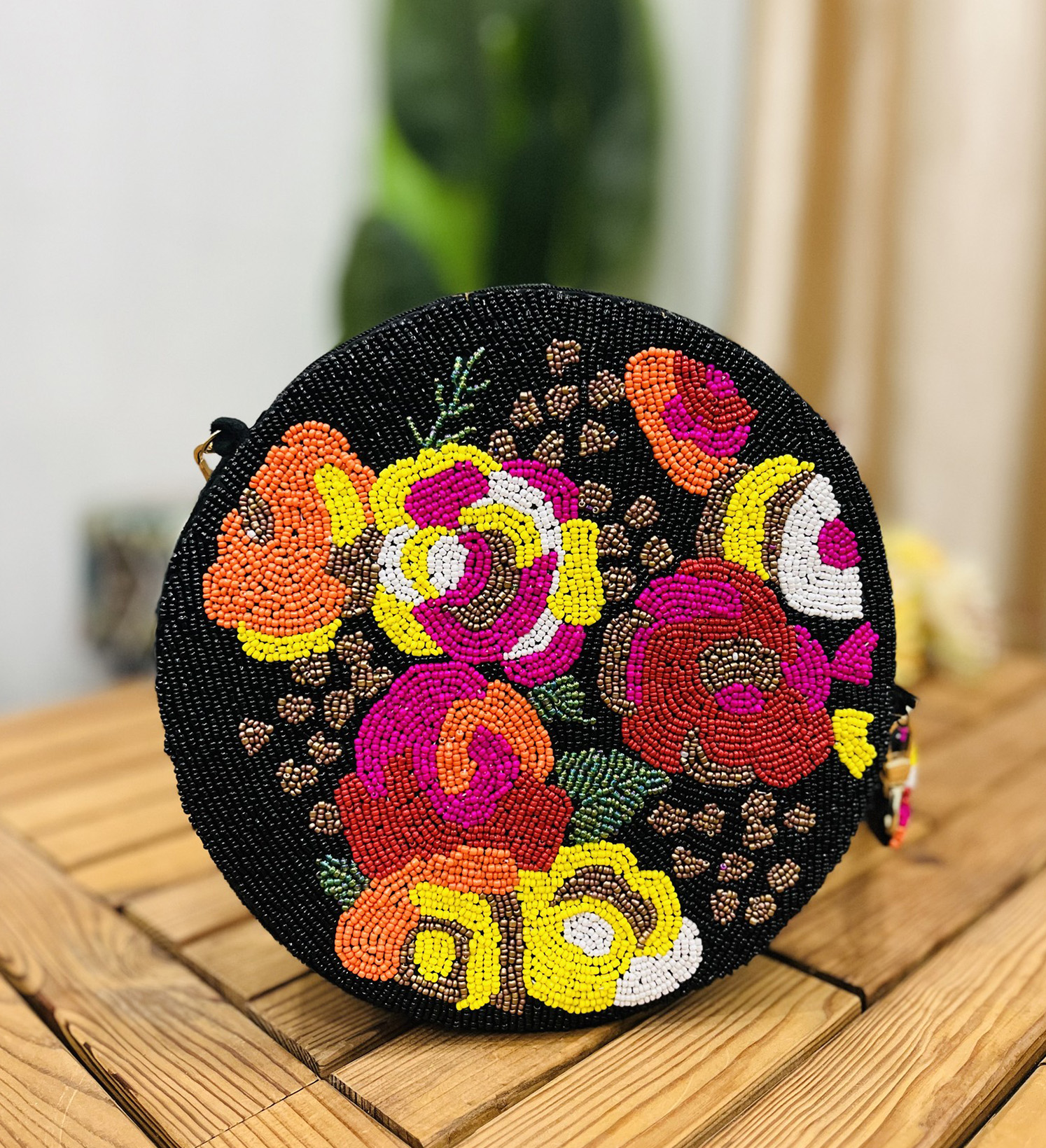 A black circular hand-beaded shoulder bag with intricate floral patterns and a chain strap, resting on a sleek, glossy