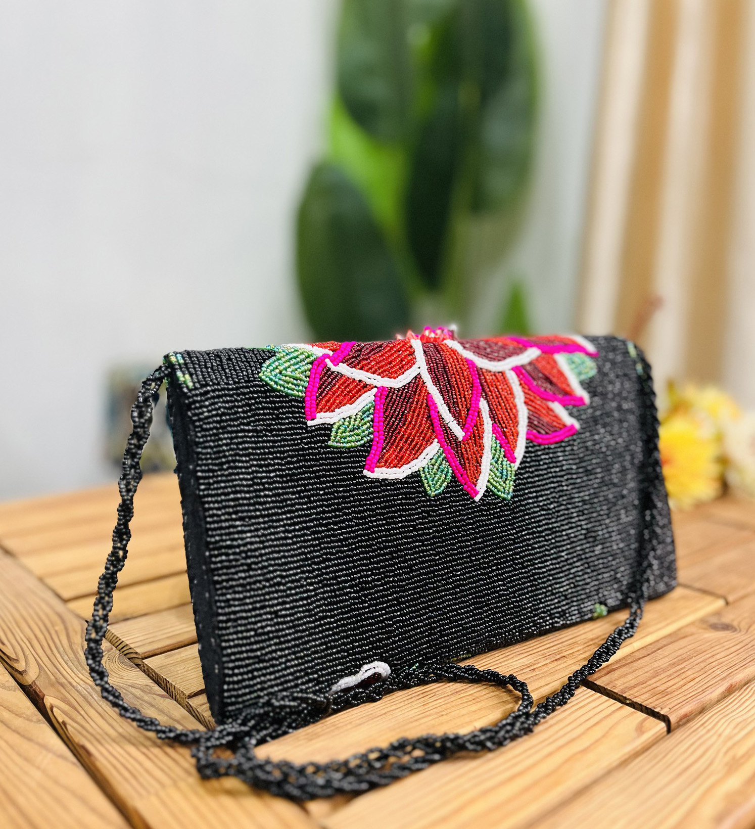 Rectangular clutch with intricate hand-beaded floral patterns in various colors on a black background, featuring a sleek
