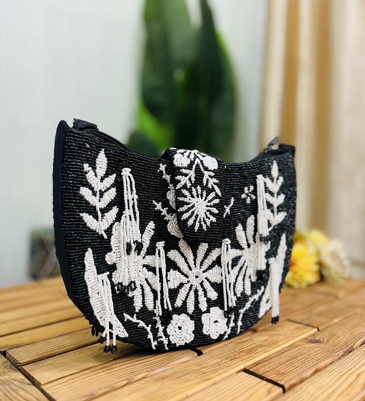 A monochrome floral hand-beaded shoulder bag featuring intricate flower designs on a textured background with a sleek strap.