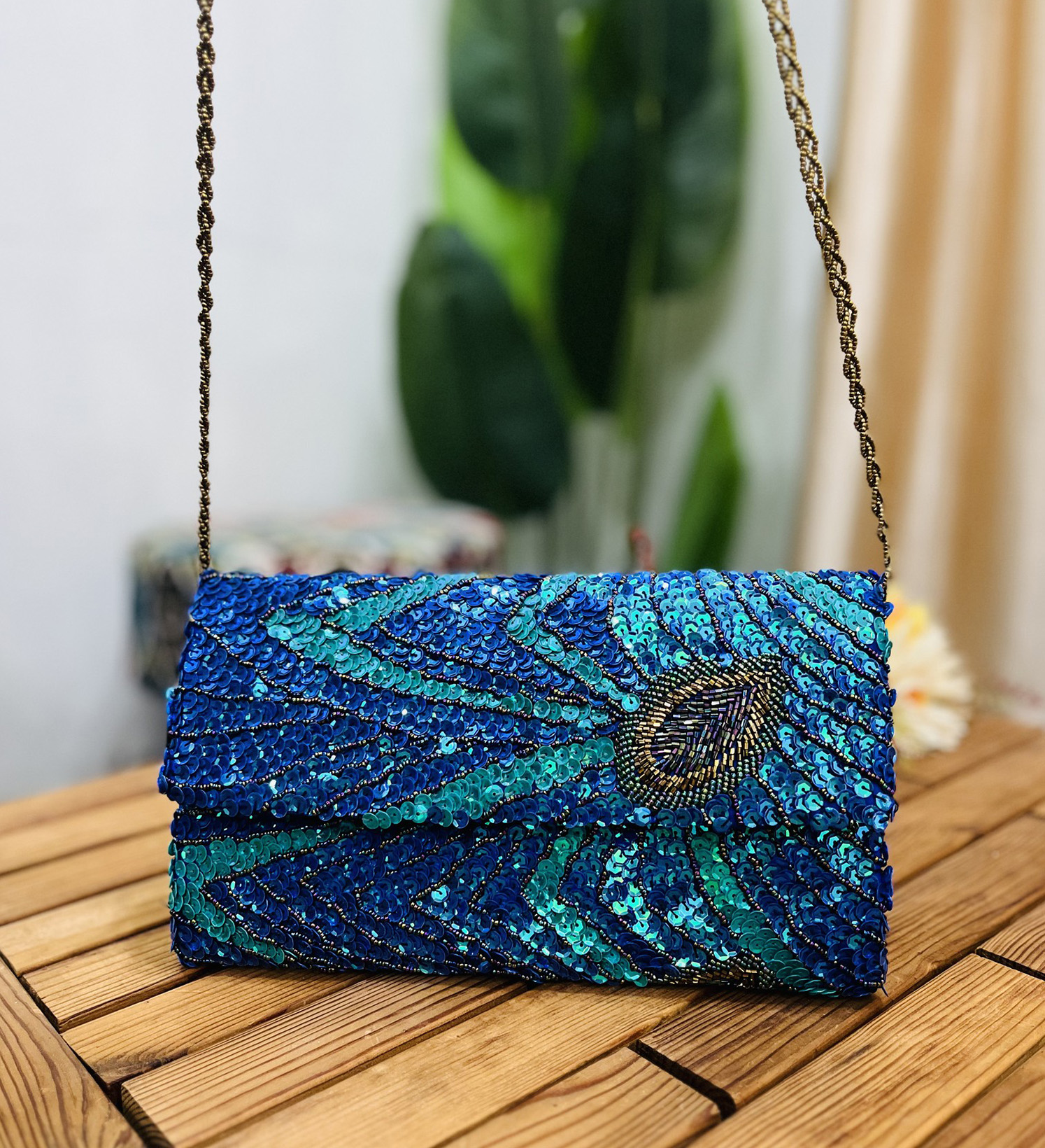 Intricately designed envelope clutch adorned with vibrant peacock feather motifs using sequins and beads on a dark