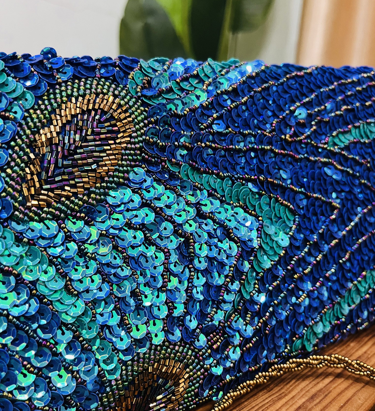 A colorful clutch with a peacock feather design, adorned with sequins and beads, set against a plain background.