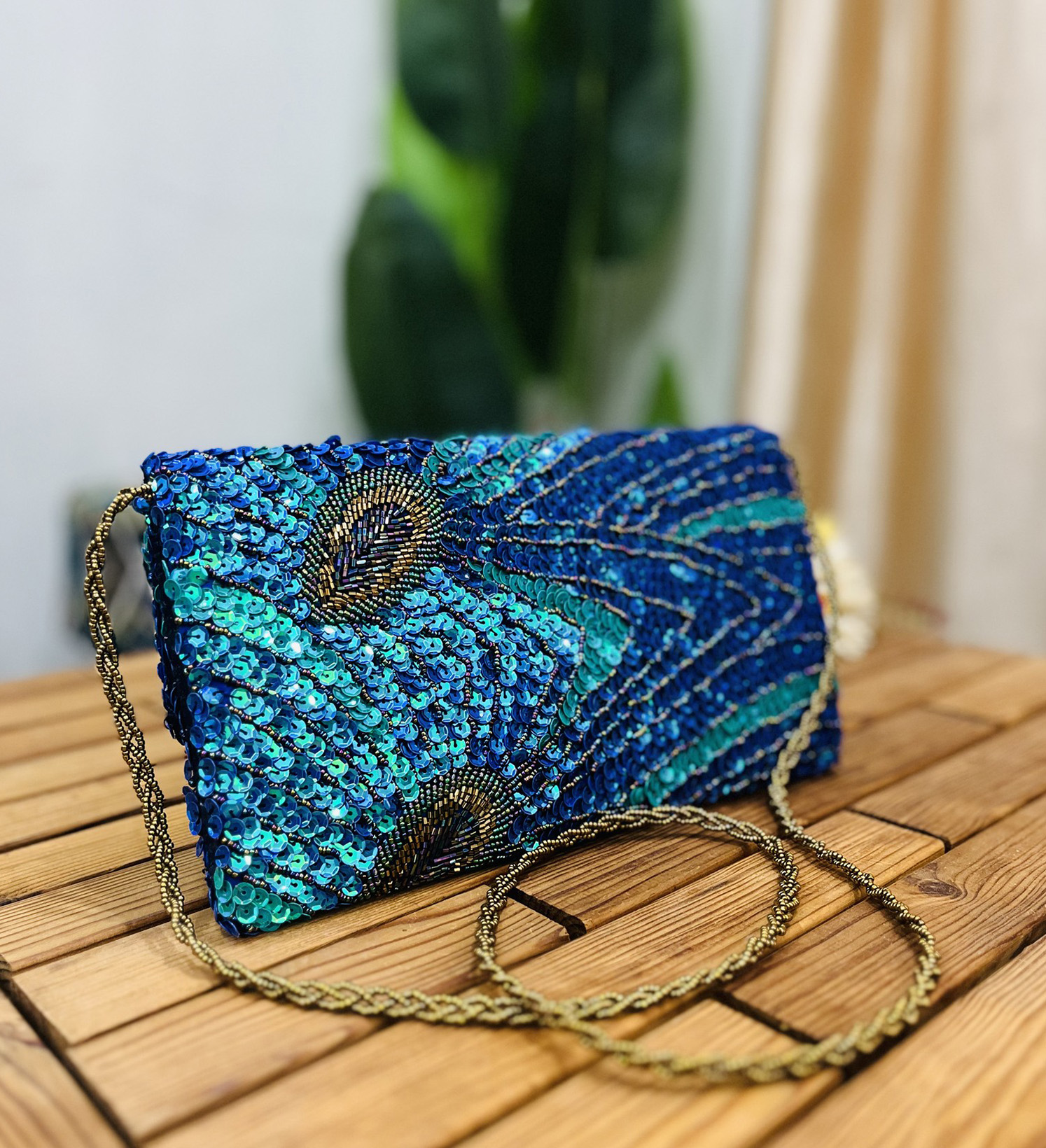 Close-up of a peacock feather-themed clutch adorned with sequins and beads, featuring intricate detailing and vibrant colors.