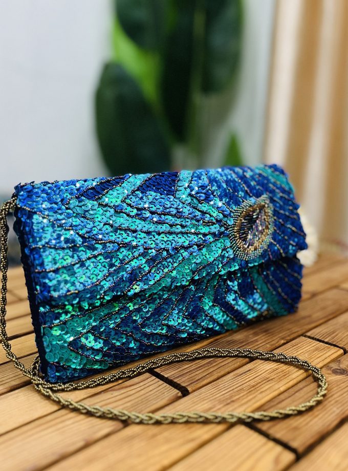 Close-up of a vibrant clutch adorned with peacock feather patterns in sequins and beads, featuring an envelope shape and