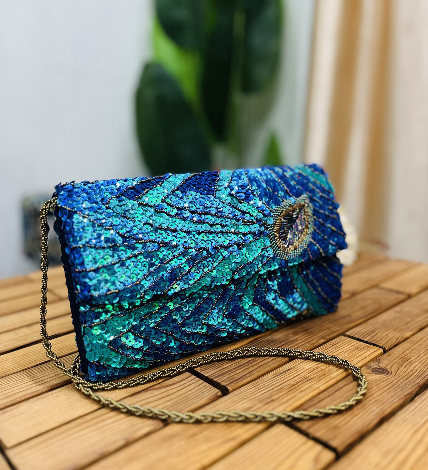 Close-up of a vibrant clutch adorned with peacock feather patterns in sequins and beads, featuring an envelope shape and